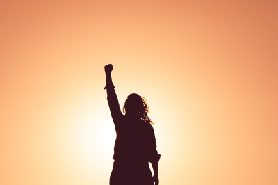 A picture of a person fist raised in celebration silhouetted in front of a sunrise