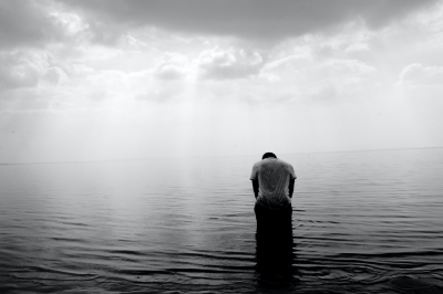 A balck and white image of a person sitting alone on a beach with their head bowed